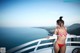 A woman in a red bikini standing on a balcony overlooking the ocean.