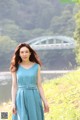 A woman in a blue dress standing by a river.