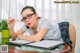 A woman wearing glasses sitting at a desk with a pen in her hand.