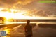 A woman standing on a beach looking at the sunset.