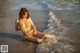 A woman in a yellow bikini sitting on the beach.