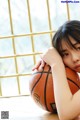 A young woman holding a basketball on the floor.